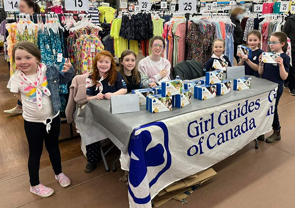 Seven girls at a table in a Walmart selling cookies.
