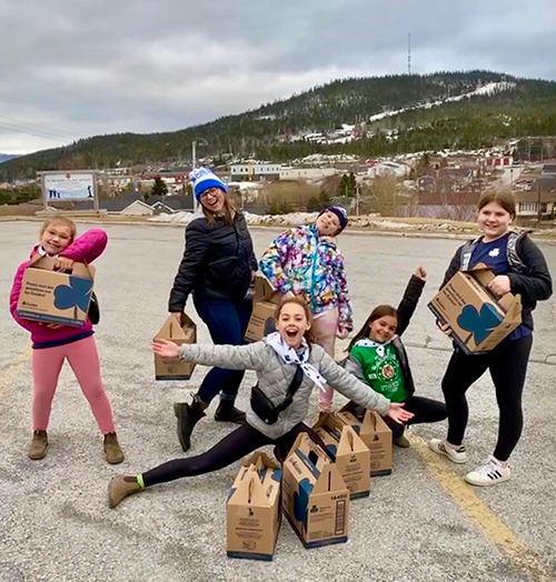 Six girls lauging with cookie cases in front of a mountain.