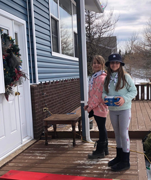 Two girls on a snowy porch with cookie boxes.