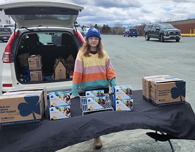 A girl selling cookies from the triunk of a car