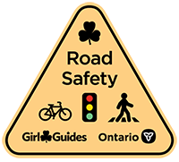 Illustration of a yellow triangular road sign with the words Road Safety, the Girl Guides logo and the Province of Ontario logo and images of a bicycle, a stop light and a pedestrian.