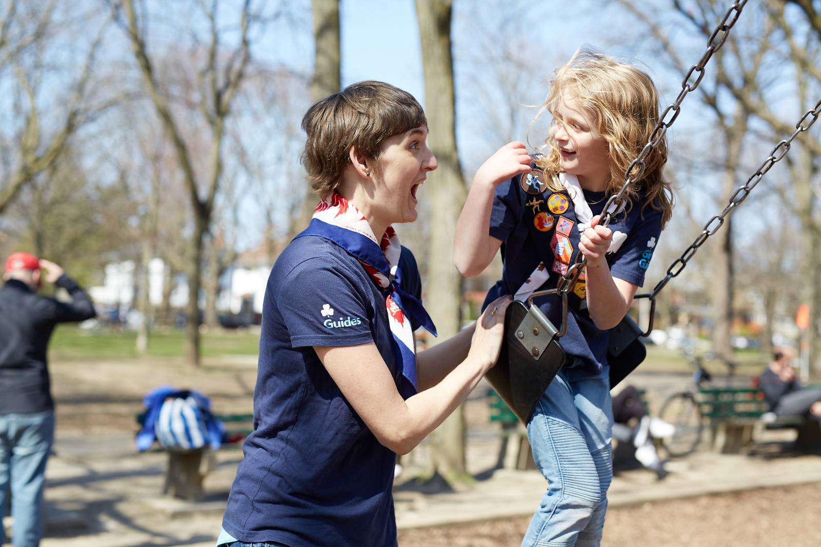 A young girl playing on a swing with a Girl Guides volunteer. The volunteer is making a face with a big smile at the girl.