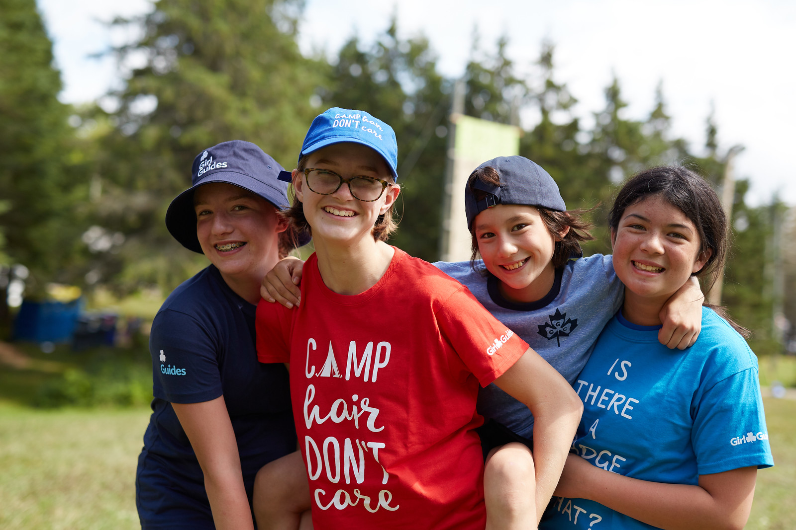 Four Girl Guides aged 9 to 11 posing together outside at summer camp. Three of the girls are lifting the fourth one on their back and shoulders.
